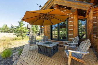 The outdoor deck at Deer Valley Oak Lodge features comfortable Adirondack chairs and a fire pit, all under the shade of a large umbrella, perfect for relaxation with a view of the surrounding landscape.