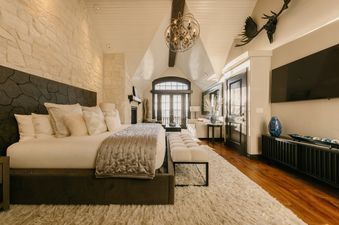 A luxurious master bedroom at Red Hawk Retreat at See Forever with a large bed, stone accent wall, vaulted ceiling, and glass doors leading to an outdoor space.
