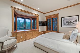 The bedroom in Silver Creek Lodge features a large bed with white bedding, a cozy armchair, and a window with a view of the surrounding trees.