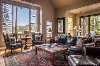 A cozy living room at Moonlight Mountain 9 Happy Trails features leather seating, a wooden coffee table, and large windows with scenic mountain views.