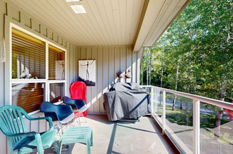 The image shows a spacious outdoor balcony at Aspens on Blackcomb Unit 332, equipped with casual seating, a BBQ grill, and an expansive view of lush green trees under natural sunlight.