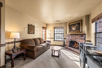The living area of Copperbottom Inn 104 features a warm and inviting atmosphere, complete with a comfortable brown sofa, a lit fireplace, and a dining table set for guests.