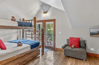 A cozy bedroom with a wooden bunk bed and a comfortable armchair.