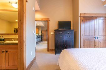 A bedroom with a dresser, TV and a bathroom to the left.