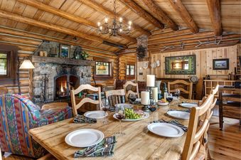 Dining table set for a meal in a cozy log cabin dining room with a stone fireplace.