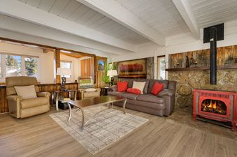 The inviting living area at 45 Idelwild features a comfortable leather sofa, armchairs, and a cozy red stove, all set against a backdrop of wooden accents and large windows.