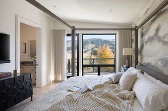 A modern master bedroom at Hidden Hollow 304 with a four-poster bed, a patterned accent wall, and a large window offering expansive views of autumn hills.