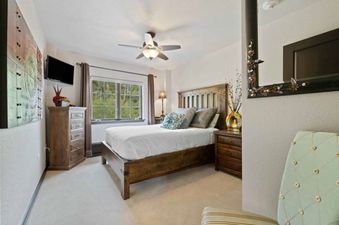 A cozy bedroom with a queen-sized bed, dresser, and a window offering a view of lush greenery.