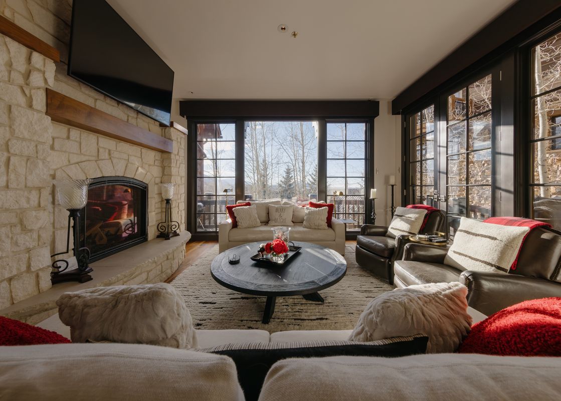A cozy and elegant living room at Red Hawk Retreat at See Forever featuring a stone fireplace, plush seating, and large windows with scenic winter views.