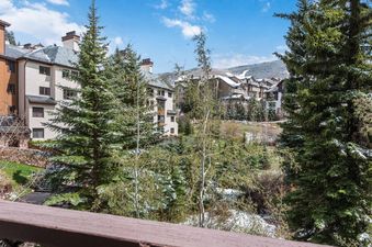 The exterior of The Charter C3305 and surrounding buildings, nestled among snow-dusted evergreen trees under a bright blue sky.