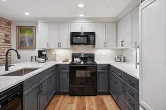 A modern kitchen in The Charter L223 featuring grey and white cabinetry, white marble countertops, and black appliances.