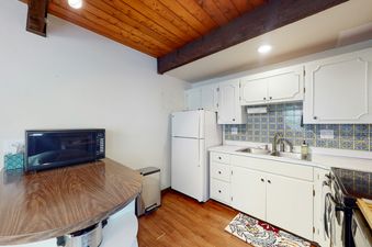 A functional kitchen with white cabinets, a blue and yellow tiled backsplash, and essential appliances such as a microwave and refrigerator.