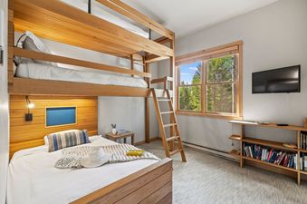 Bunk bedroom at Moose Creek 15 with custom wooden bunk beds, a large window showing green trees, and a wall-mounted TV.