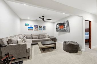 A modern and cozy basement family room at Snowline at Black Rock Ridge with a gray sectional sofa, coffee table, beanbag chairs, and a wall-mounted TV.