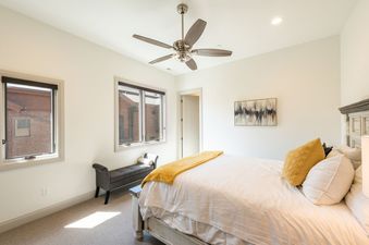 The serene bedroom at Juniper 801 features a bed with white and yellow bedding, two windows, and a ceiling fan.