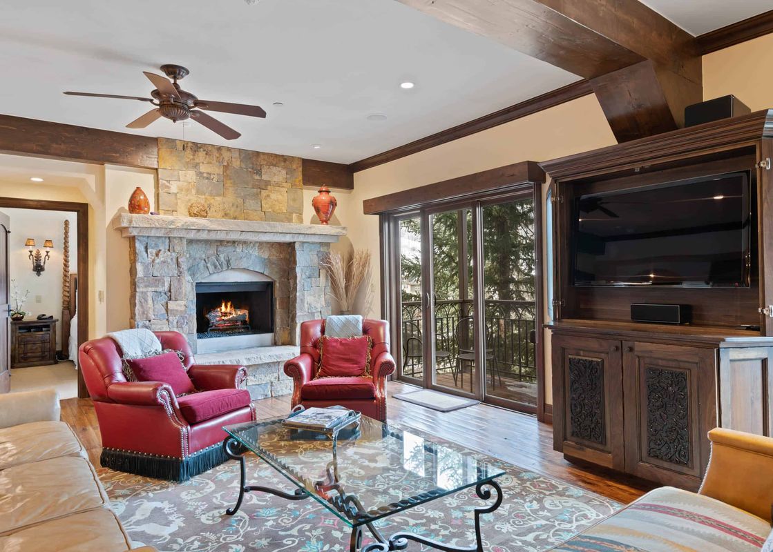 A cozy living room in The Charter E340 with a stone fireplace, red armchairs, a glass coffee table, and a view of the balcony through sliding glass doors.
