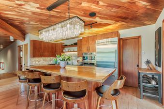 Modern kitchen with a large island, wooden cabinets, and a chandelier.