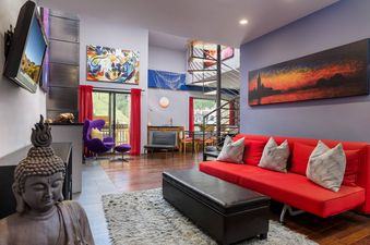 A vibrant living room at Vail 21 601 features a red sofa, a purple egg chair, colorful artwork, and a modern spiral staircase, with glass doors opening to an outdoor view.