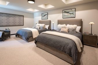 A serene bedroom in The Lodge Cabins Six Bedroom Mountain Cabin features two twin beds with grey bedding, cozy throws, and fluffy pillows, flanked by elegant nightstands with lamps.