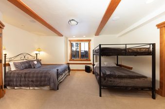 The Timber Trail Lodge bedroom features a king-sized bed with an ornate metal headboard, plaid bedding, and two bedside lamps.