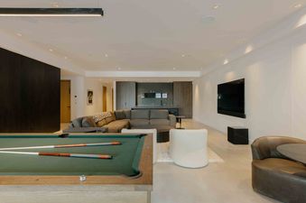 A modern basement living area with a pool table, leather chairs, and a large sectional sofa.