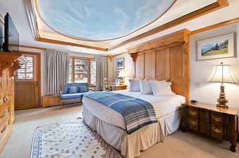 A luxurious king bedroom in Lodge Tower 387 3BR with elegant wooden furnishings, a blue settee, and a large window offering an exterior view.