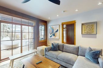 The living room of Settlers Lodge 104 with a large sectional couch facing a coffee table. There is a large window in the background that leads to a view of the snowy mountains and trees.