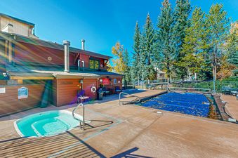 The outdoor pool and hot tub at Phoenix 107 are surrounded by a wooden building with a grassy area behind it.