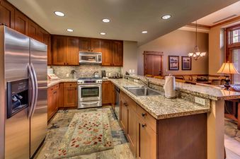 A modern kitchen with stainless steel appliances, wooden cabinets, granite countertops, and a breakfast bar.
