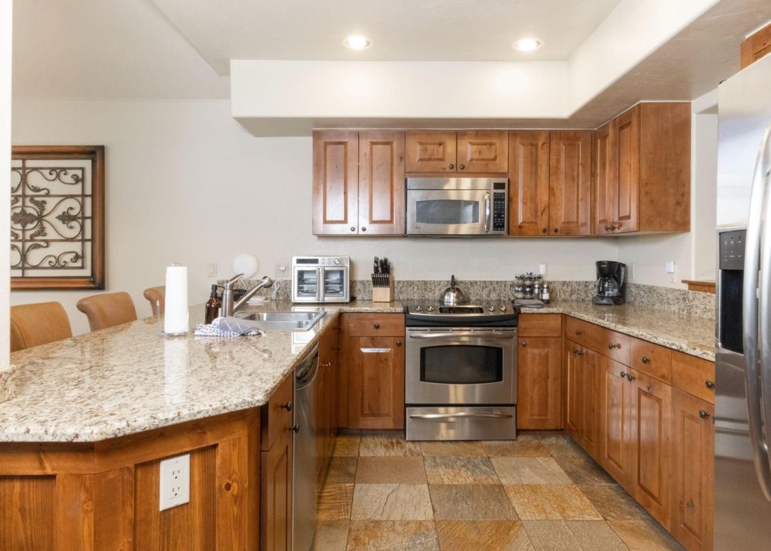 The kitchen at Villa at Mountain Thunder features a spacious granite countertop, wood cabinetry, and stainless steel appliances, including a microwave, oven, and refrigerator.