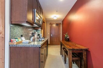 A kitchen with stainless steel appliances and granite countertops in a condo with a wood table and chairs in the hallway.