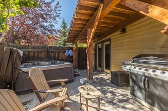An inviting outdoor patio at Essentia Townhome 145A with a hot tub, BBQ grill, and seating under a pergola.