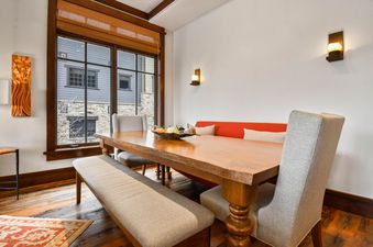A close-up shot of the dining area in Arrowleaf Lodge 302, featuring a long, rustic wooden table, an upholstered bench, and plush chairs, with decorative wall sconces providing warm lighting.