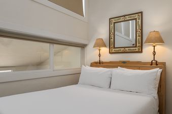 A cozy bedroom with a queen-sized bed, two bedside lamps, and a decorative mirror hanging above the wooden headboard.
