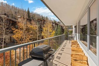 A private balcony at Lodge Tower 387 3BR with a BBQ grill and firewood, overlooking a mountain landscape with autumn trees.