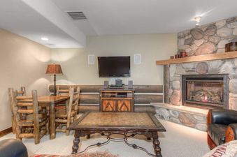 A cozy lounge area with a stone fireplace, a rustic dining table, a television, and comfortable seating.