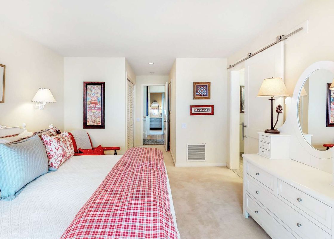 The bright and inviting bedroom with a plaid and floral bedspread, a white dressing table, and decorative wall art.