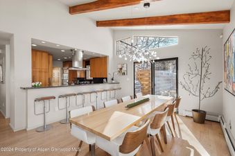 A modern dining room with a large wooden table, six white chairs, and a beautiful chandelier hanging above.