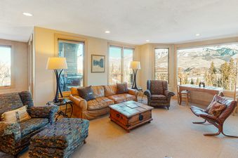 Lorian 14 offers mountain views from the living room. The living room features a leather sofa, two armchairs, a coffee table, and two floor lamps.