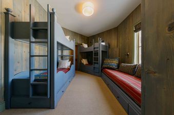 A cozy bunk room at Elk Lake Lodge features multiple bunk beds and a comfortable window seat, all crafted from dark wood with rustic wooden wall paneling.