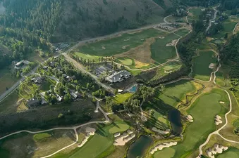 An aerial view captures the extensive golf course, residential area, and resort amenities, including a swimming pool, all set against a backdrop of mountains.