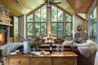 A cozy mountain living room at Teton Grove with a stone fireplace, large cathedral windows, and comfortable leather seating.