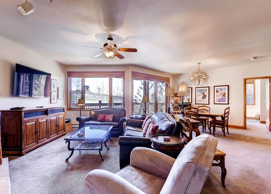 A spacious and comfortably furnished living and dining area in Christie Club 316, featuring leather seating and views of the surrounding slopes.