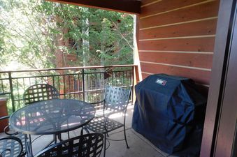 The balcony at Moose Creek 35 features a patio table with chairs, a covered grill, and a view of surrounding trees.