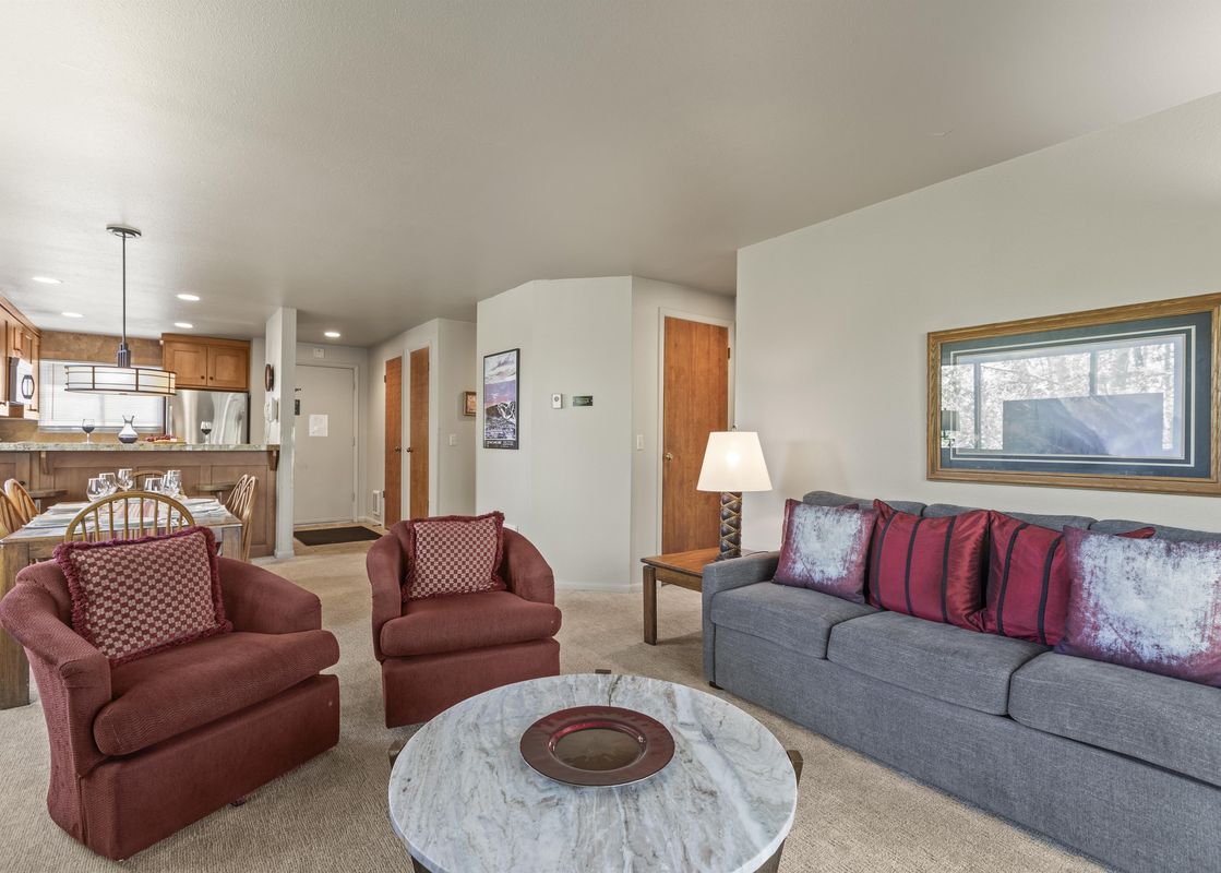 The inviting living area of Snow Flower 140 Park City features a gray sofa, two burgundy armchairs, a marble coffee table, and a dining area, all within an open-concept layout.