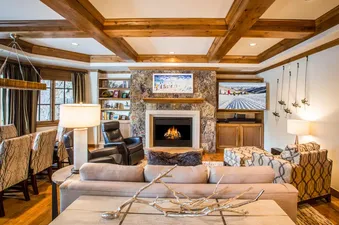 An elegant and warm living room in Chateau Beaver Creek Residence 1304, featuring a stone fireplace, large TV, comfortable sofas, and wooden accents, creating a cozy and luxurious atmosphere.