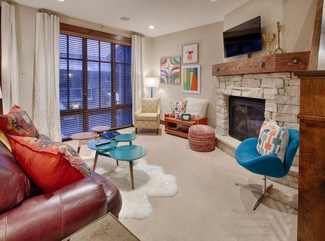 The vibrant living area of Silver Star 702, featuring a red leather sofa, colorful accent chairs, a stone fireplace, and large windows with wooden blinds.