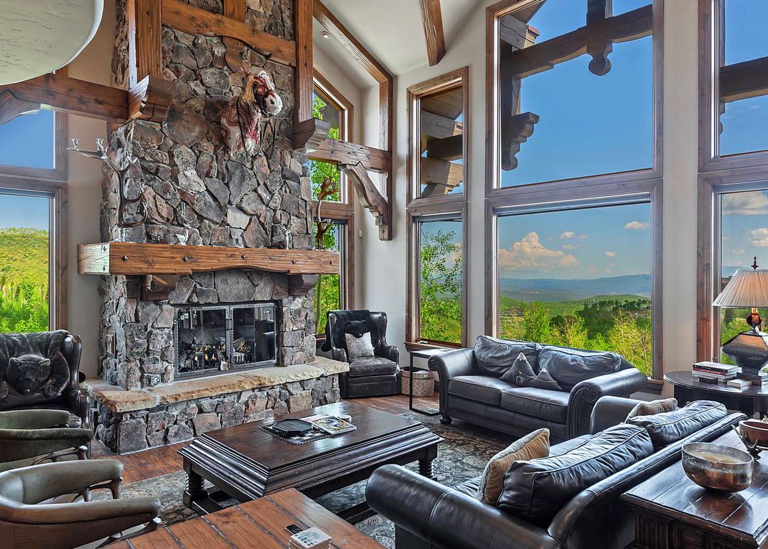 A spacious living room featuring a grand stone fireplace, comfortable seating, and large windows offering panoramic mountain views.