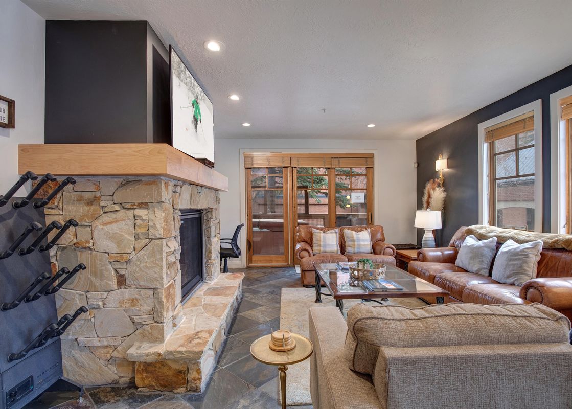 A spacious living room at Town Pointe A105 featuring a large stone fireplace, comfortable sofas, and a television above the mantel, perfect for relaxing after a day outdoors.