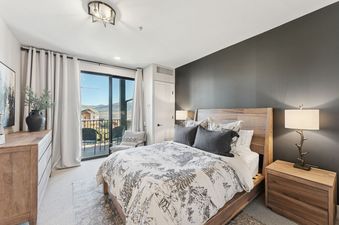 A large bedroom with a wooden bed, a large balcony with a view of the mountains, and a rustic dresser.